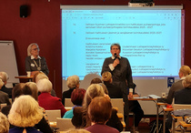 Kuvassa mikrofoni kädessä liiton uusi puheenjohtaja toimikaudelle 2025 - 2027 Merja NIeminen Kouvolan Seudun Lottaperinneyhdistyksestä